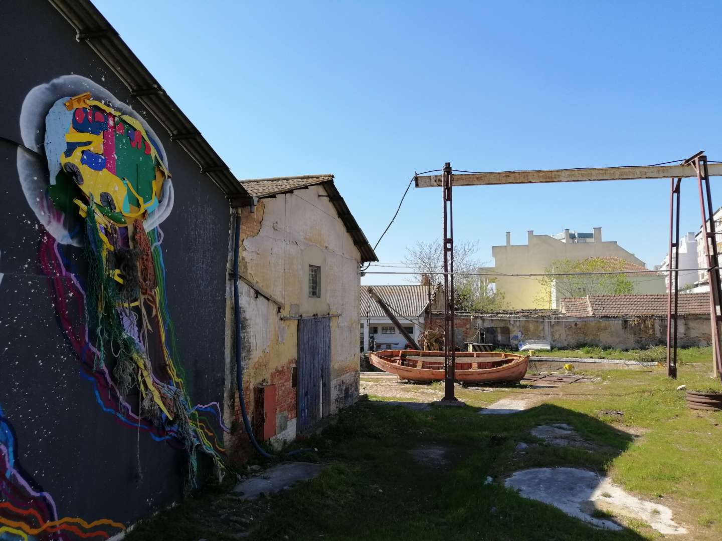 Calle abierta de Barreiro con casas en ruinas, un bote abandonado y una pintada colorida en una pared.
